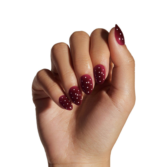 Berry polka dot press-on nails displayed on model's hand against white background