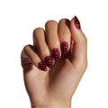 Berry polka dot press-on nails displayed on model's hand against white background