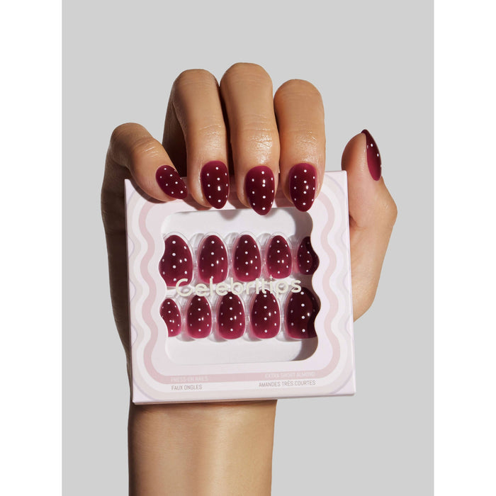 Woman holding Berry Polka Dot press-on nails package, displaying burgundy nails with white dots