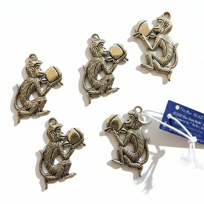 Five monkey-shaped metal charms on a gray surface with a blue tag.