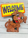 A colorful outdoor decoration featuring a cartoon dog holding a 'Welcome' sign.