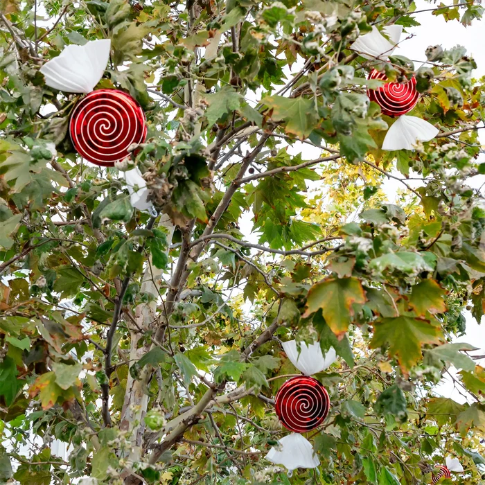 Decorative spiral lollipop ornaments and white paper wings hanging on the branches of a leafy autumn tree.