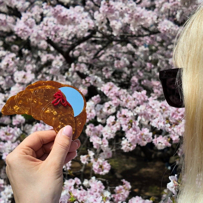 Hand-painted bow croissant compact mirror held up against blooming pink flowers