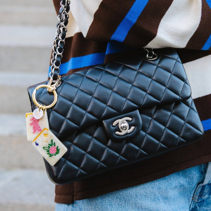 Black quilted Chanel bag with hand-painted flower mahjong charm, styled with striped ribbon strap