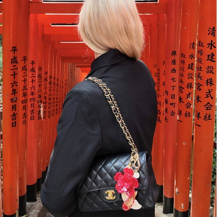 Black quilted bag with red koi fish charm attached to gold chain strap, worn by woman at red temple gate