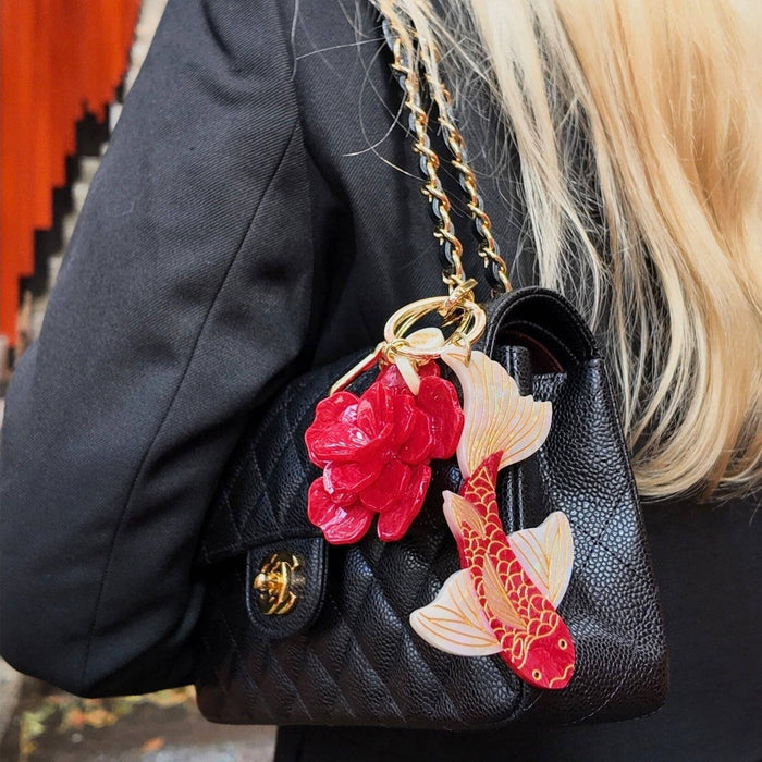 Hand-painted koi fish bag charm with red and gold details attached to black leather handbag