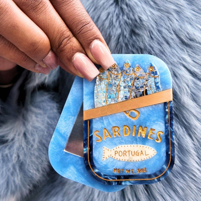 Hand-painted sardines compact mirror held in manicured hands with blue fur background